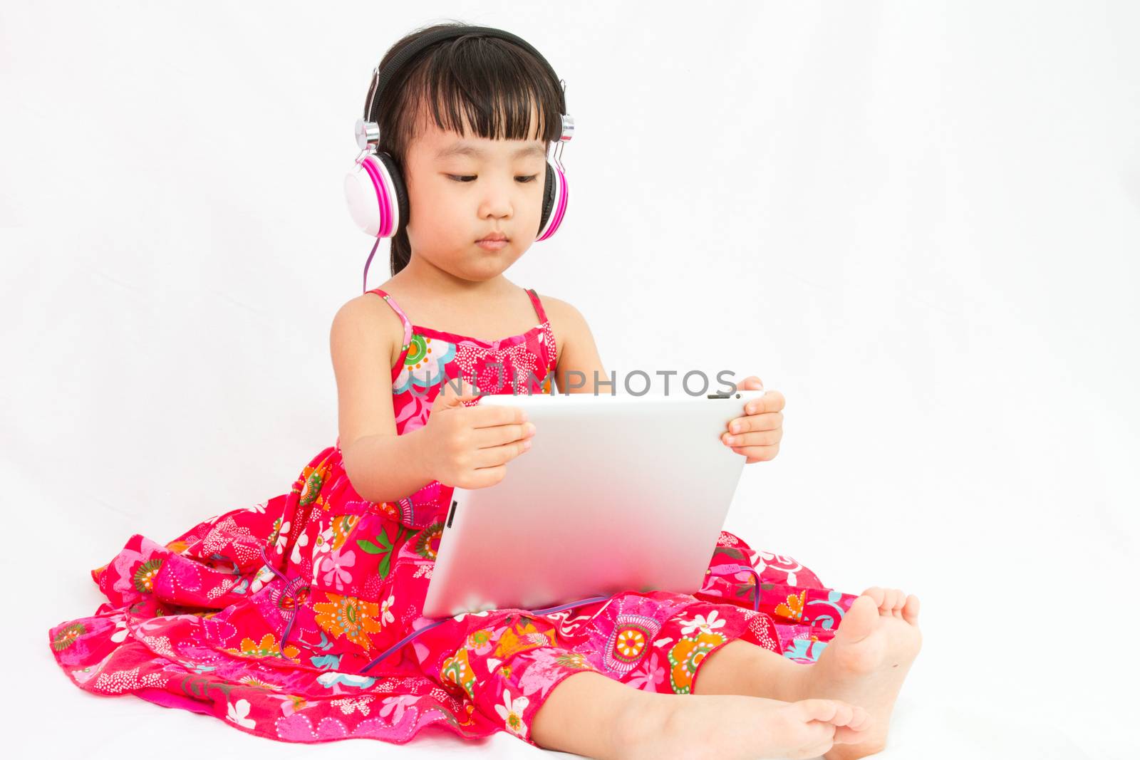 Chinese little girl on headphones holding tablet in plain isolated white background.