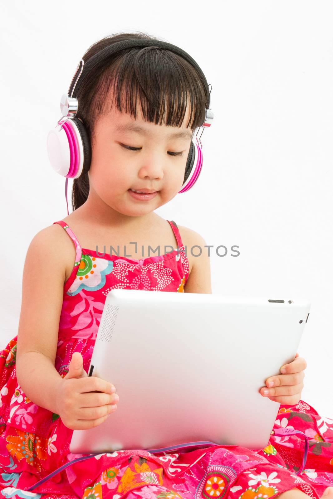 Chinese little girl on headphones holding tablet in plain isolated white background.