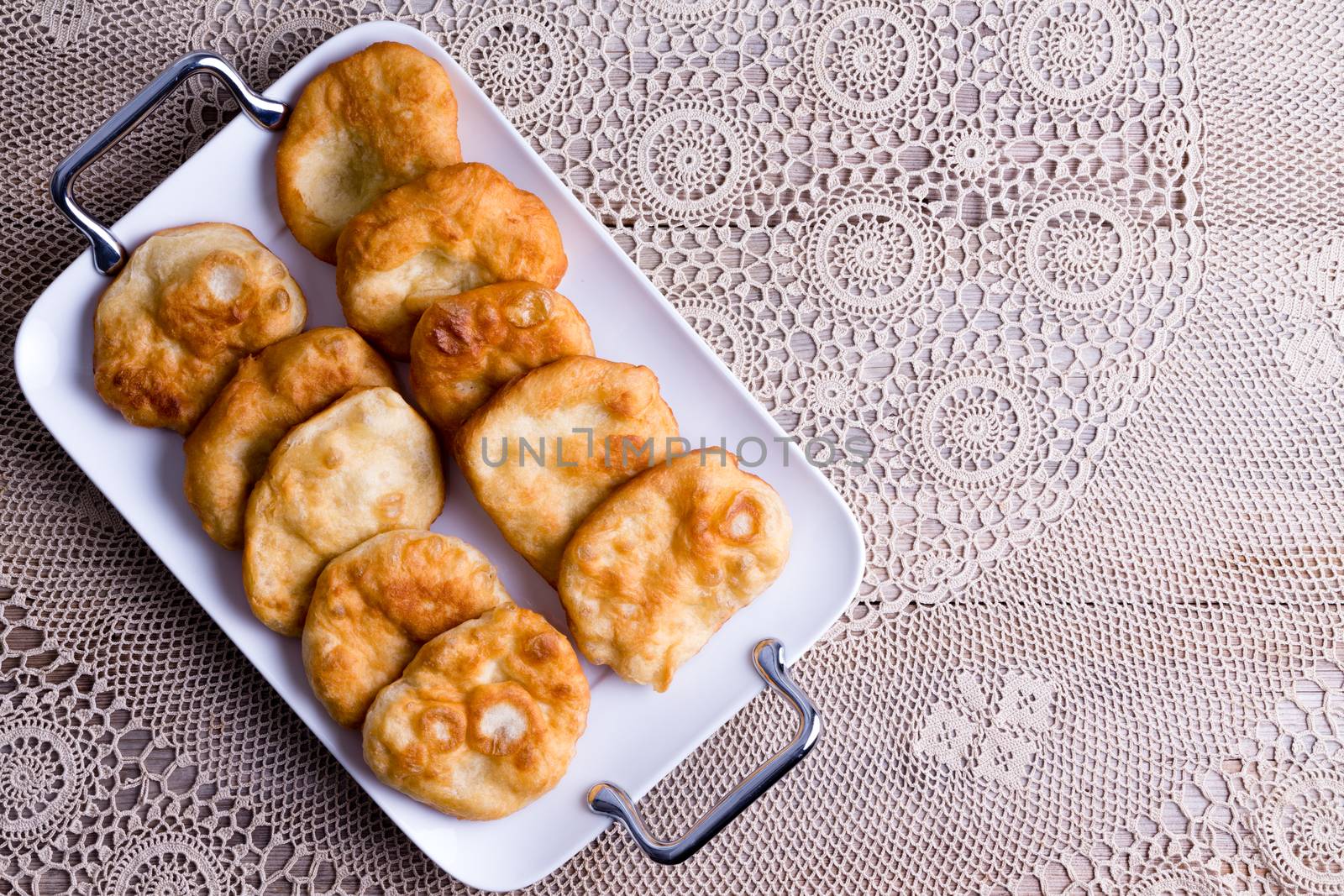 Tray of traditional fried Turkish pisi halka, or fried dough crumpets, served on an old table with a lace tablecloth and copy space, overhead view