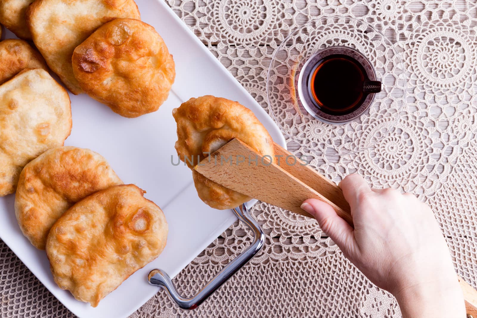 Woman serving delicious traditional Turkish pisi halka or fried dough with a cup of Turkish tea, view from overhead of her hand with wooden tongs serving from a tray