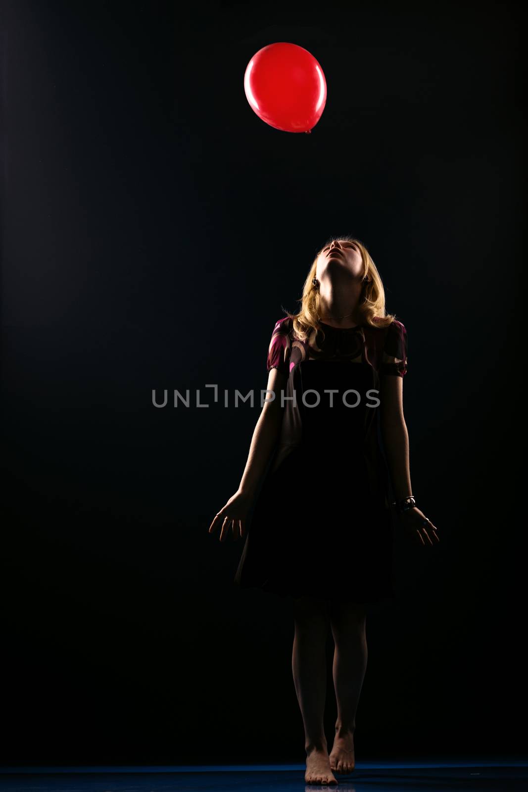 Concept: dream, sadness, hope. Barefoot girl reaching for the flying balloon isolated on black background