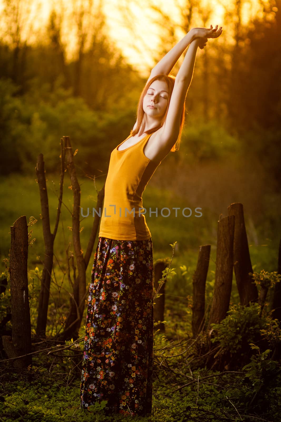 Beautiful redhead girl casually walking under the rays of the sunset in summer forest