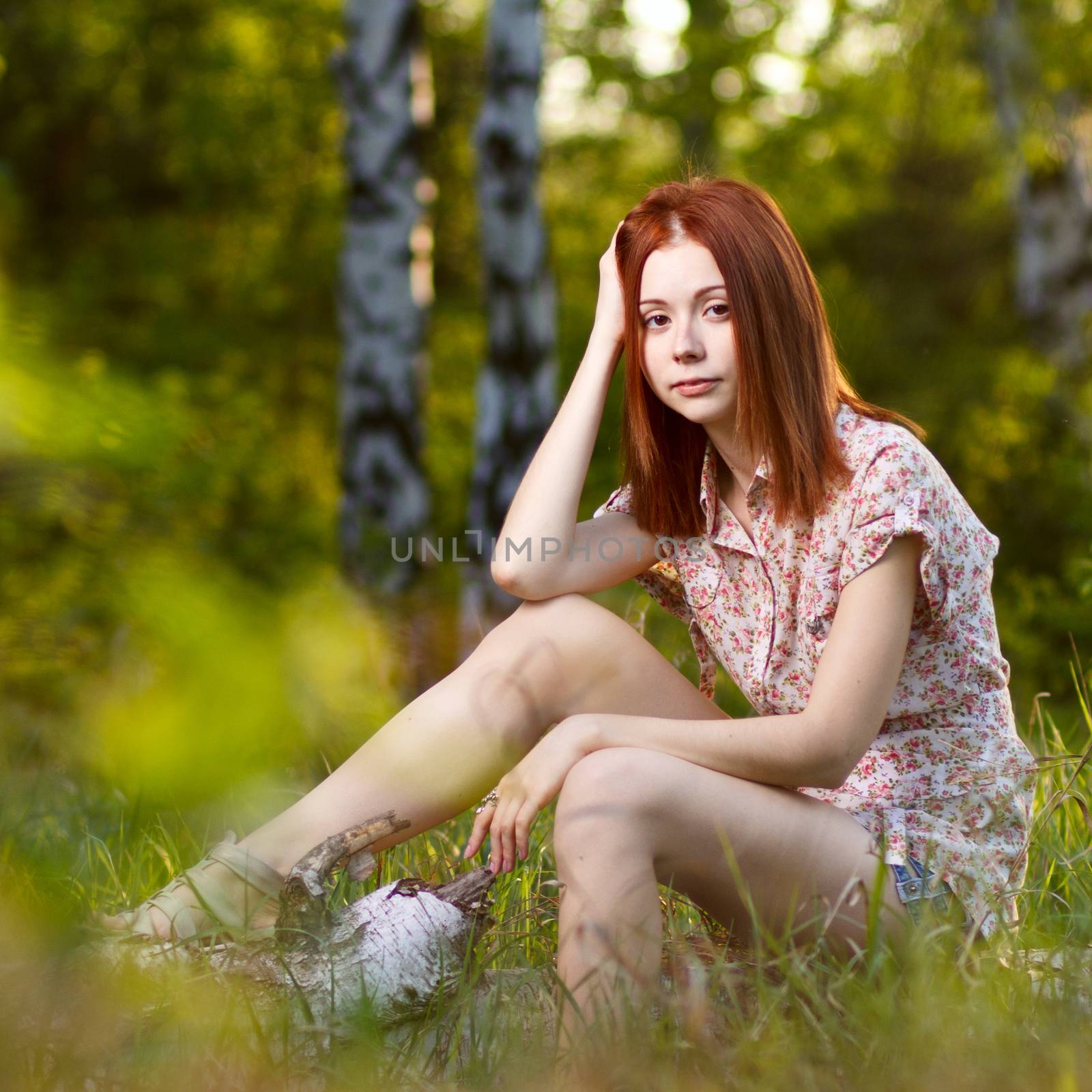 Beautiful redhead girl walking under the rays of the sunset in summer spring forest