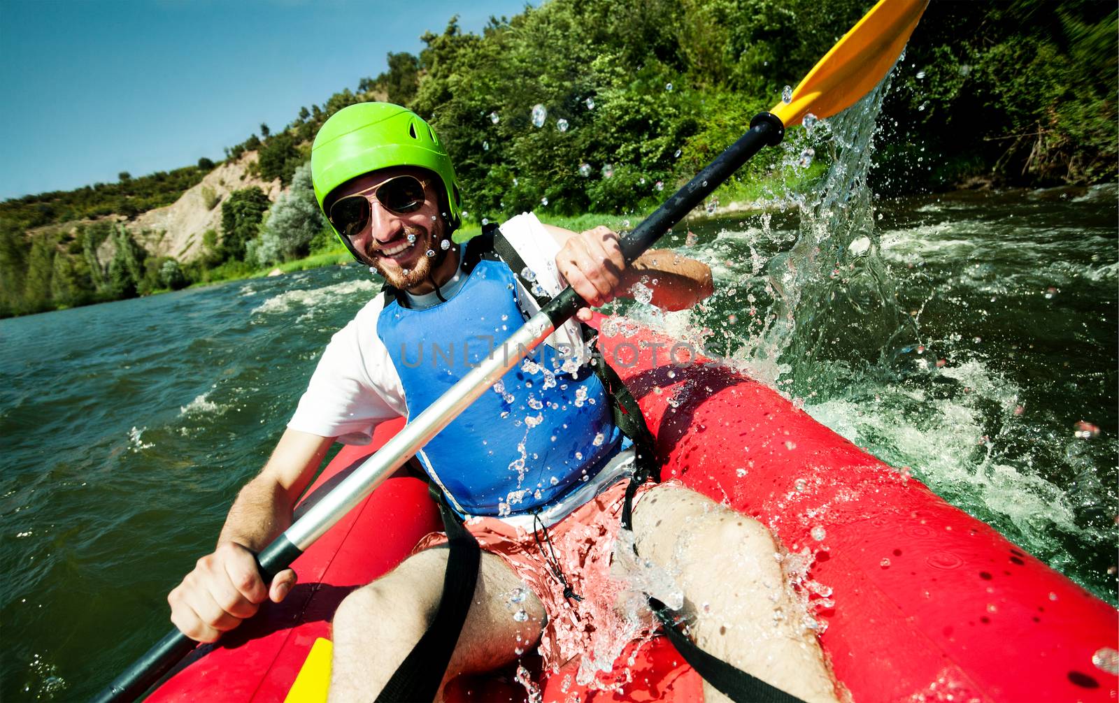 A happy entusiastic male in red inflatable canoe having a fun ride in calm waters of a river.