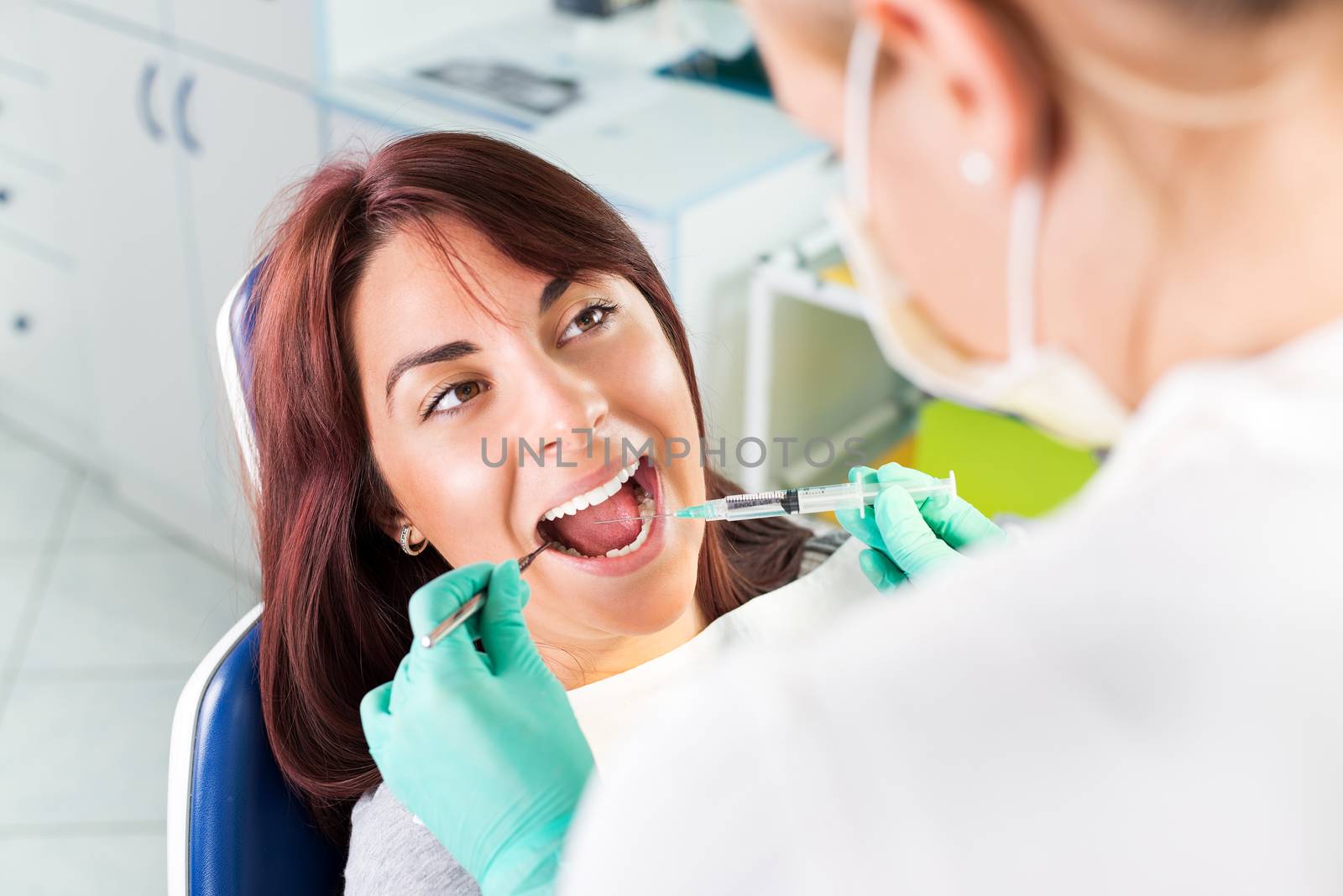 Young female dentist giving anesthesia to the patient before dental surgery. Selective focus, focus on the patient.