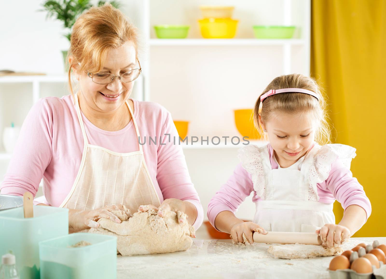 Beautiful happy grandmother and her granddaughter making Dough and rolling pin in the kitchen.