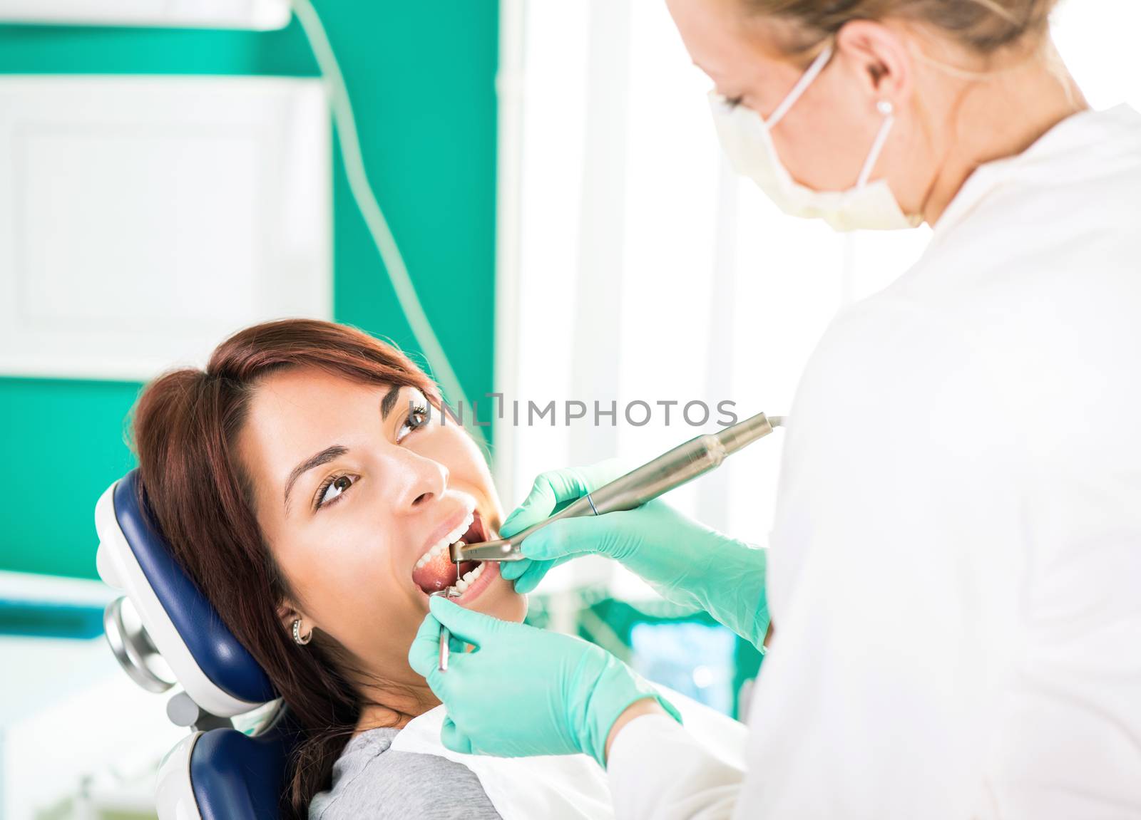 Female dentist with dental drill repairing tooth on the female patient in the office.