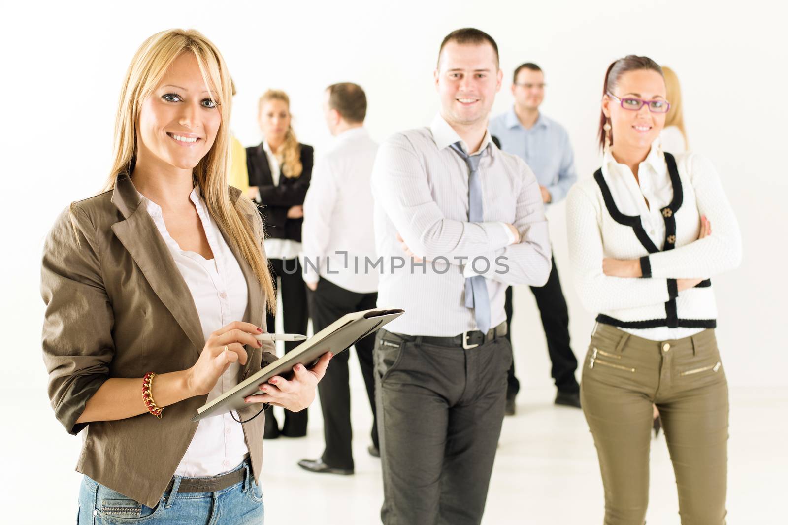 Smiling businesswoman standing in front of colleagues with crossed arm and looking at the camera.