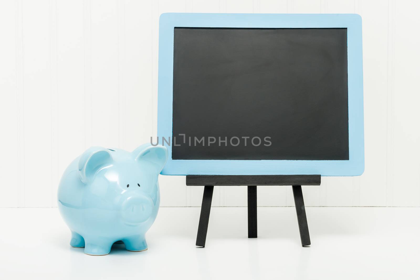 Blue porcelain piggy bank beside a blank chalkboard.  Ample copy space.