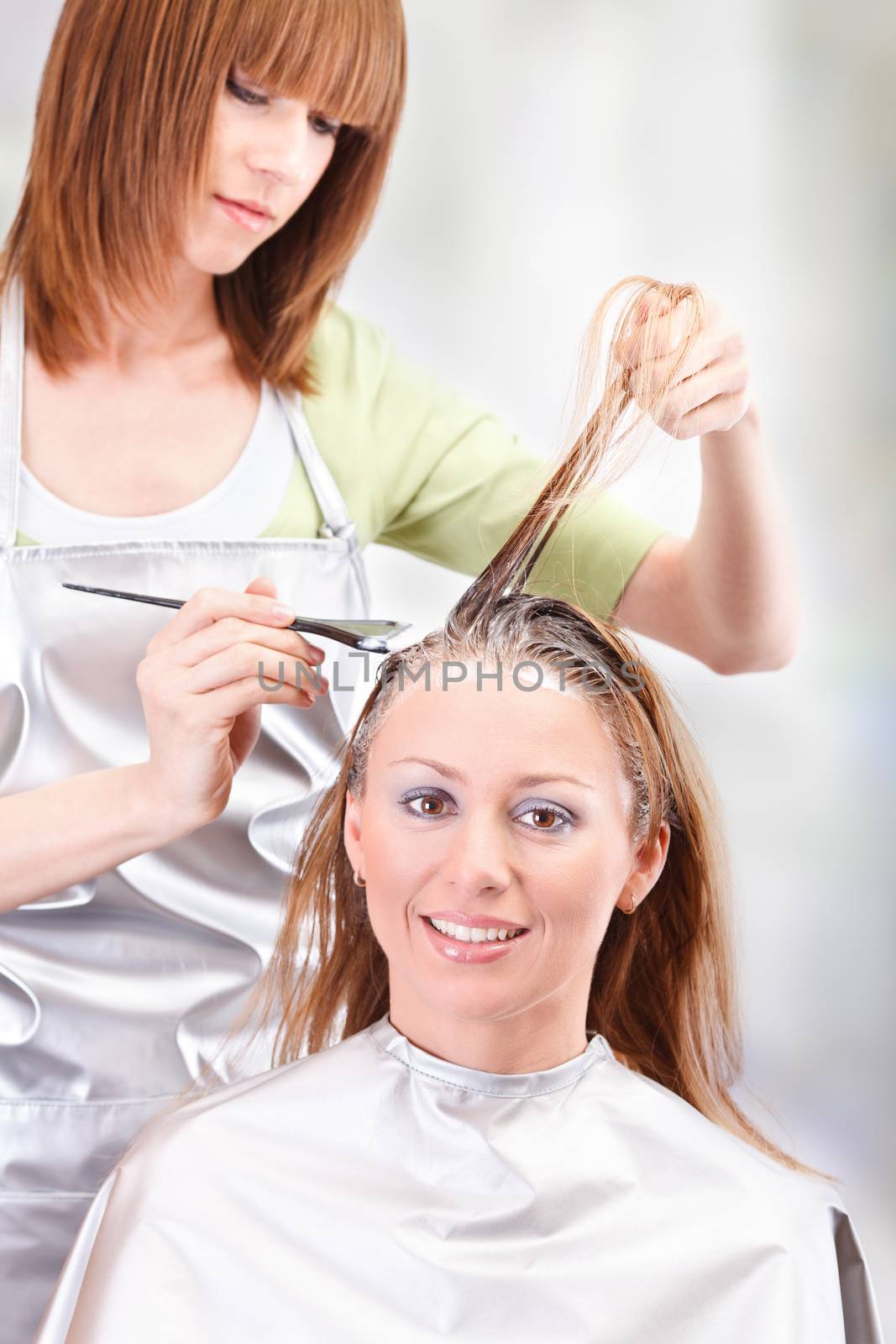 Young beautiful hairdresser coloring hair with hair color
