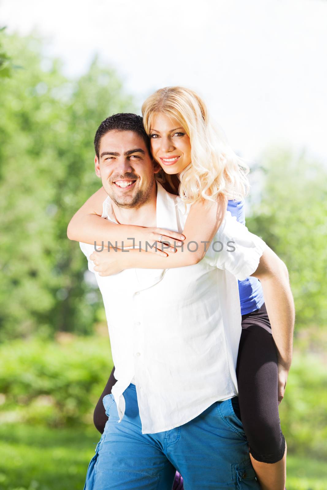 Young man Carrying On Shoulders a beautiful girl in nature