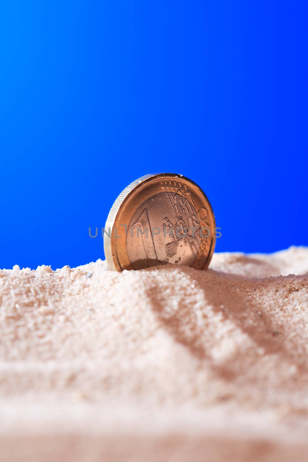 One Euro coin in sand against blue background