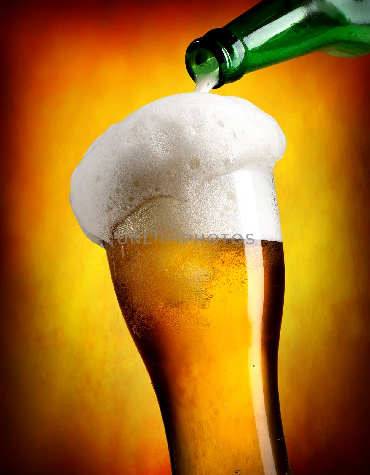 Beer pouring from bottle in tumbler on orange background