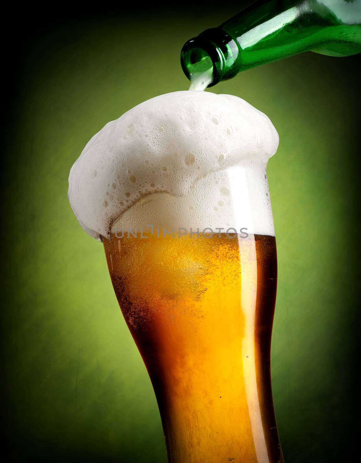Beer pouring into glass on green background