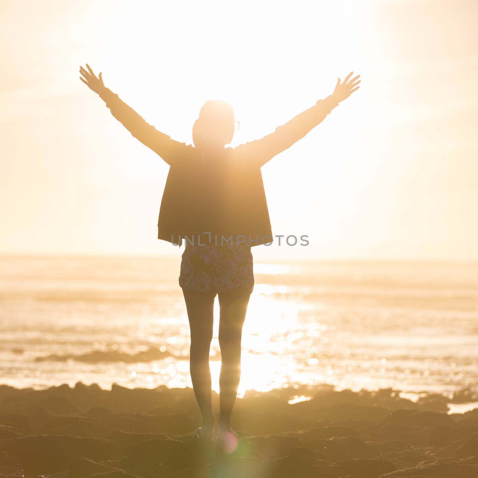 Silhouette of free woman enjoying freedom feeling happy at beach at sunset. Serene relaxing woman in pure happiness and elated enjoyment with arms raised outstretched up. 