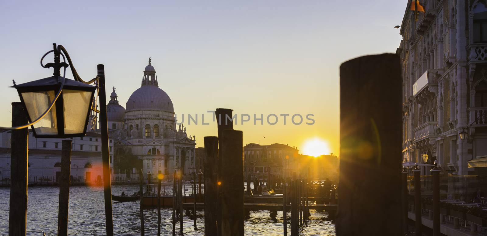 Romantic Italian city of Venice in sunset. World Heritage Site. Traditional Venetian wooden boats, gondolier and Roman Catholic church Basilica di Santa Maria della Salute.