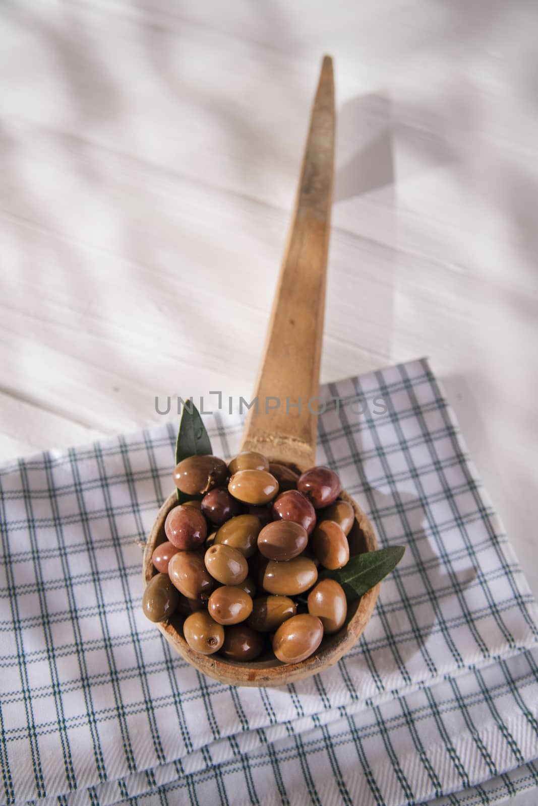 Presentation of a small group of black olives on wooden ladle
