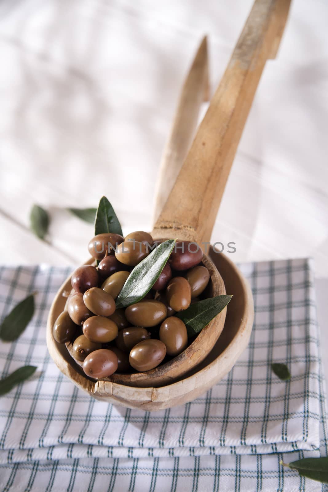 Presentation of a small group of black olives on wooden ladle
