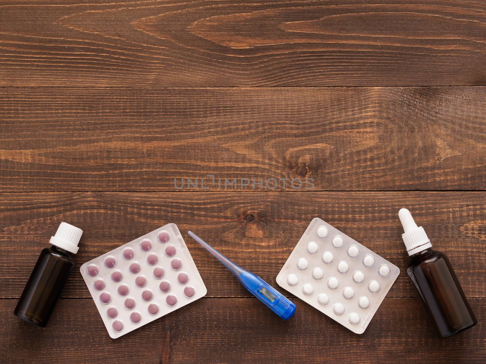 medications and thermometer on a wooden background by fascinadora