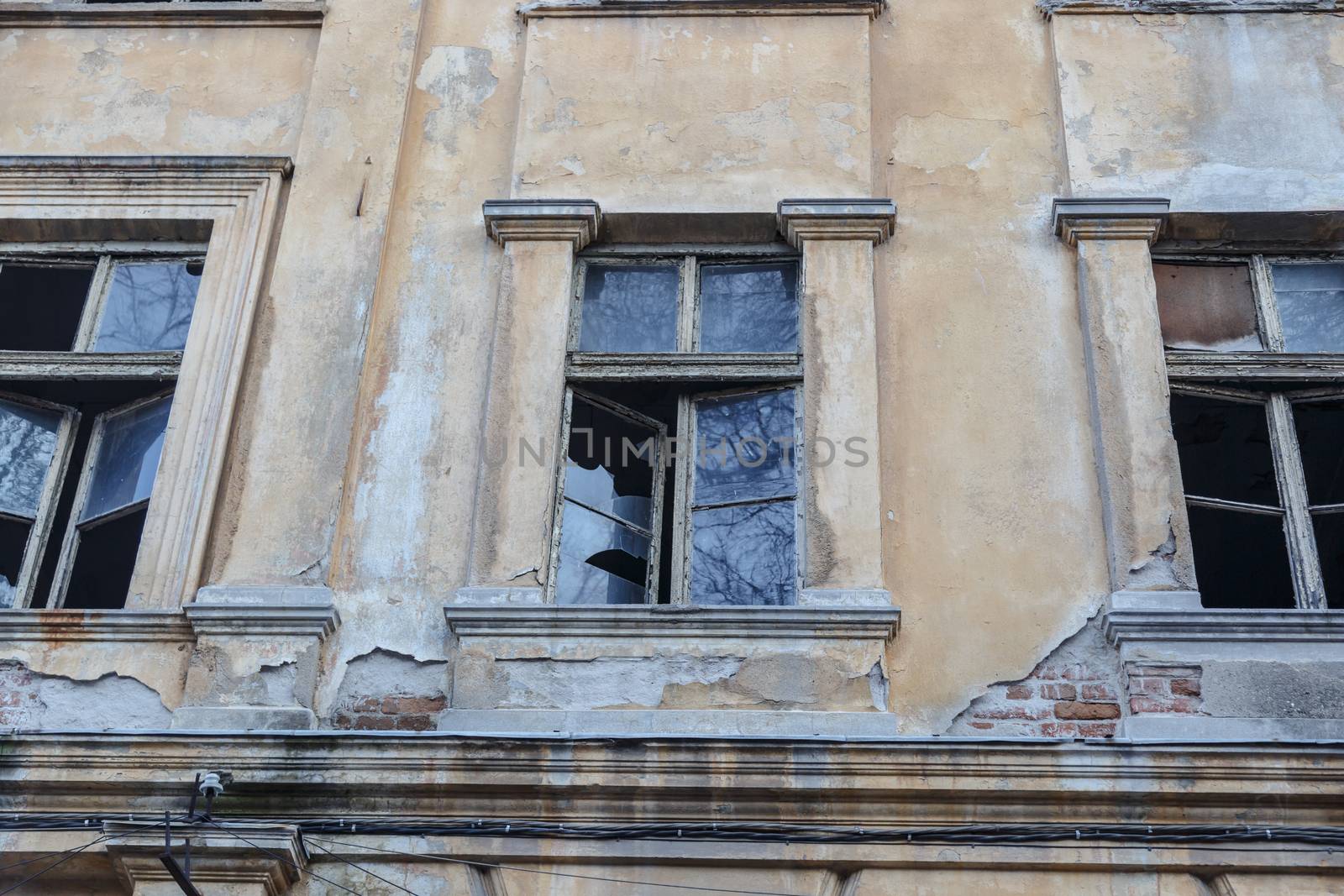 Bottom view of destroyed abondoned yellow stone building with broken windows.