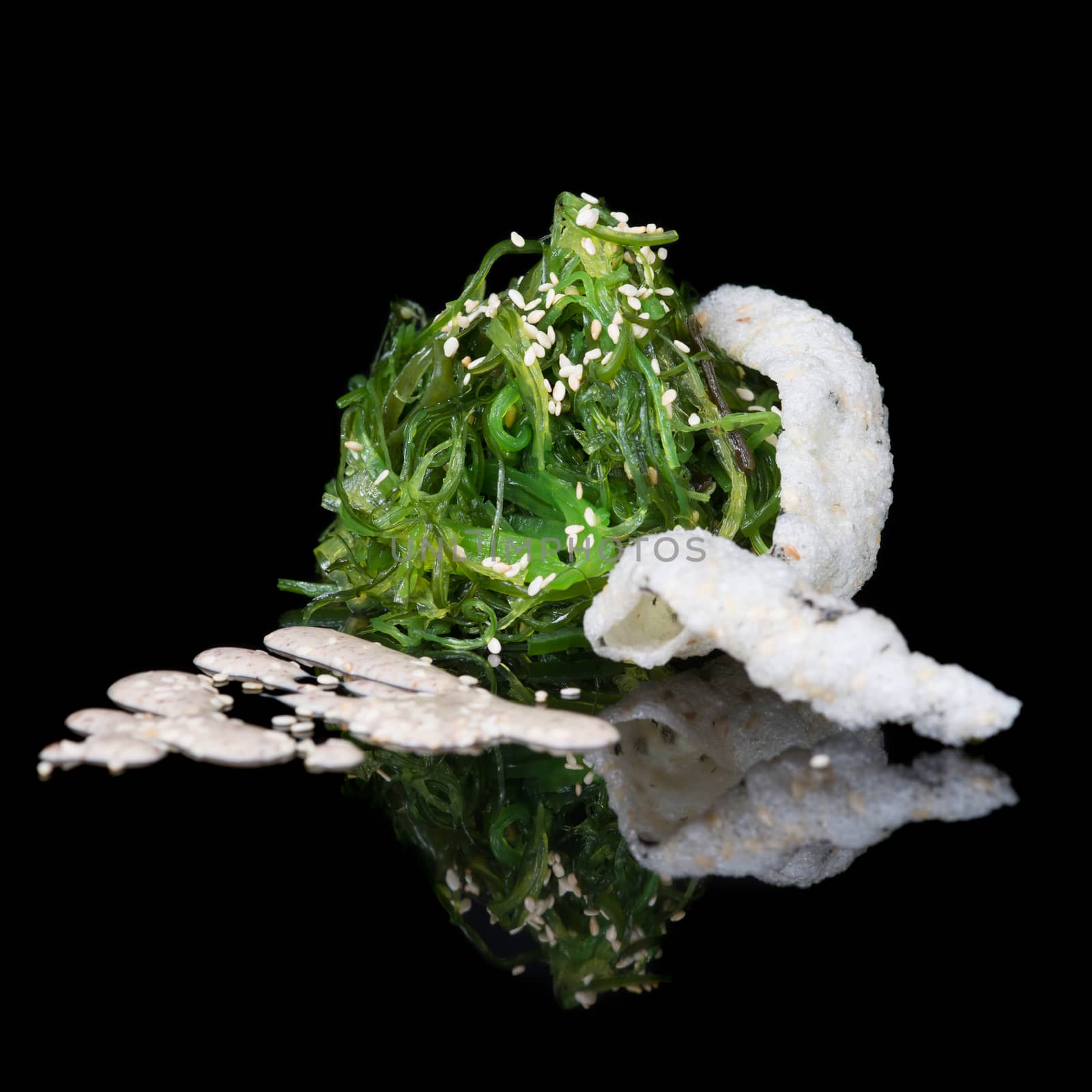 Sesame seaweed salad with rice chips on black background