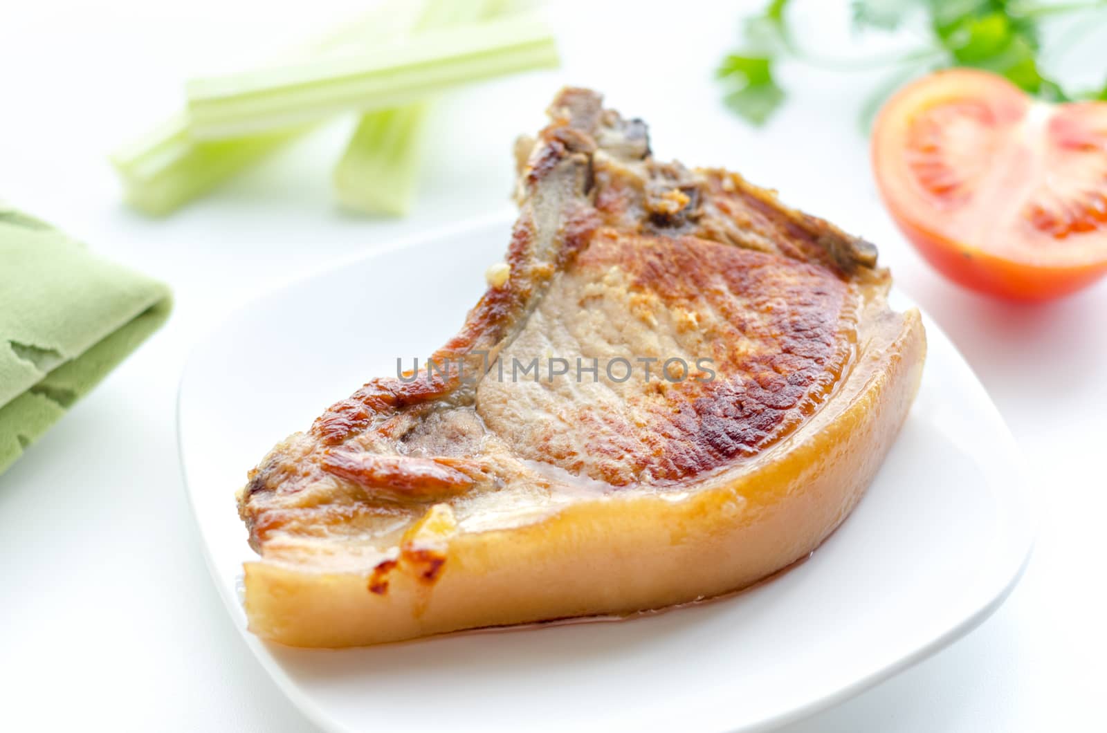 Roast pork in a bowl, morning and bokeh. On rostkoviana background, green cloth, half of tomato,slices of celery and parsley