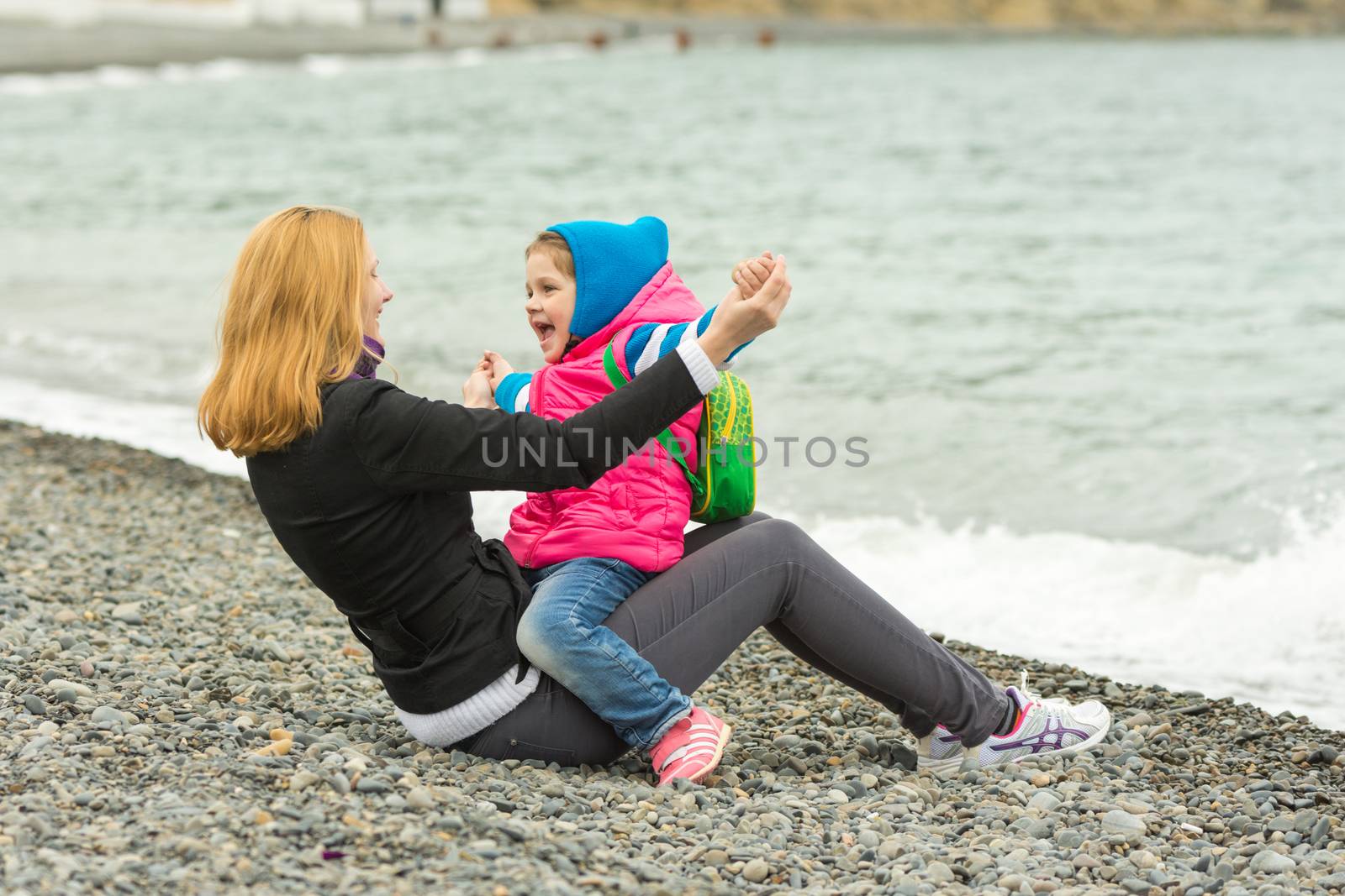 Mom and daughter having fun playing while sitting on the beach on a cool day by Madhourse