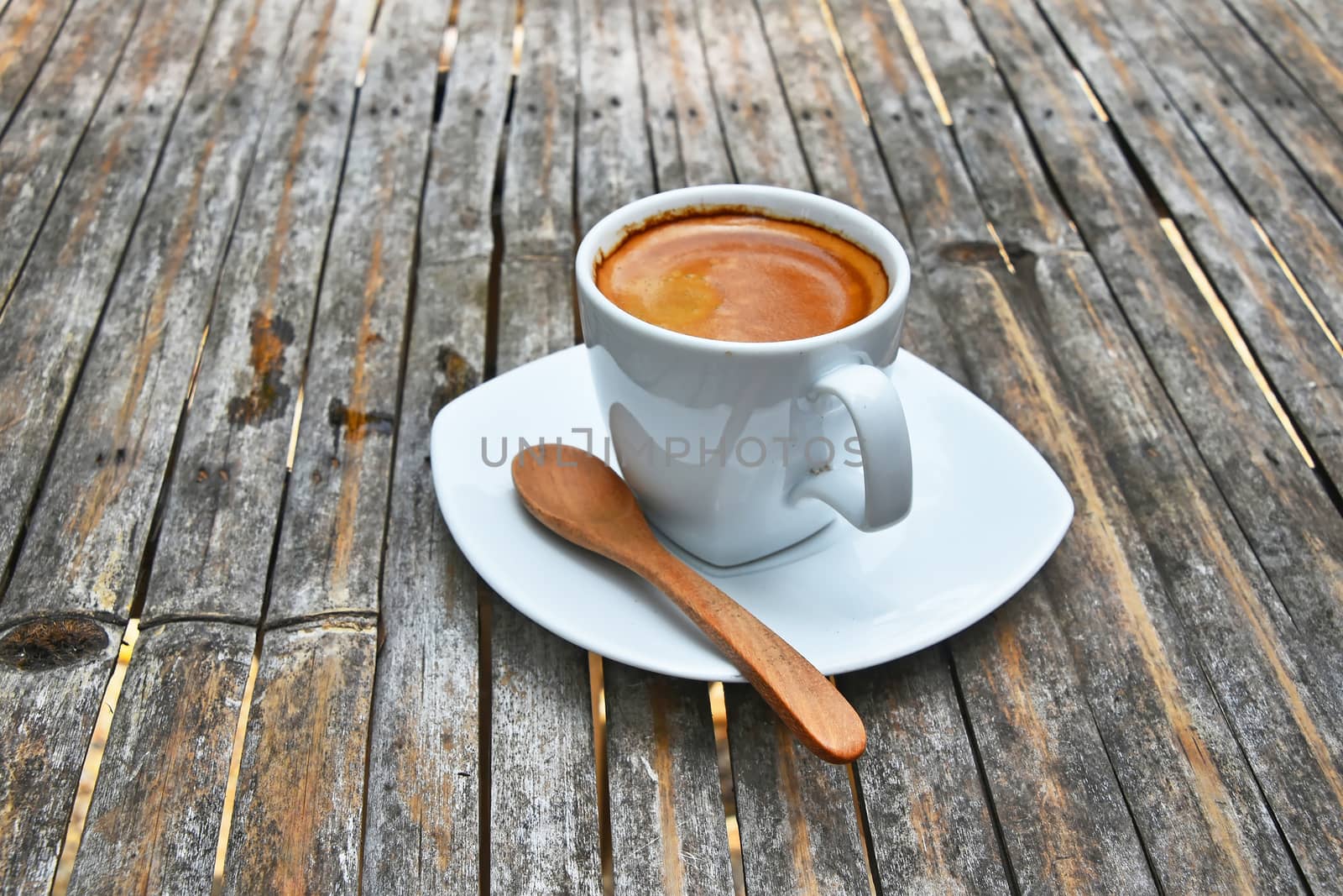 One white cup full of espresso coffee with brown crema on porcelain saucer with wooden spoon on old vintage bamboo table