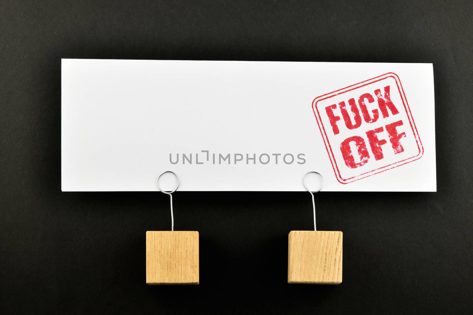 Fuck off red rude stamnp on one big white paper note with two wooden holders isolated on black paper background for presentation