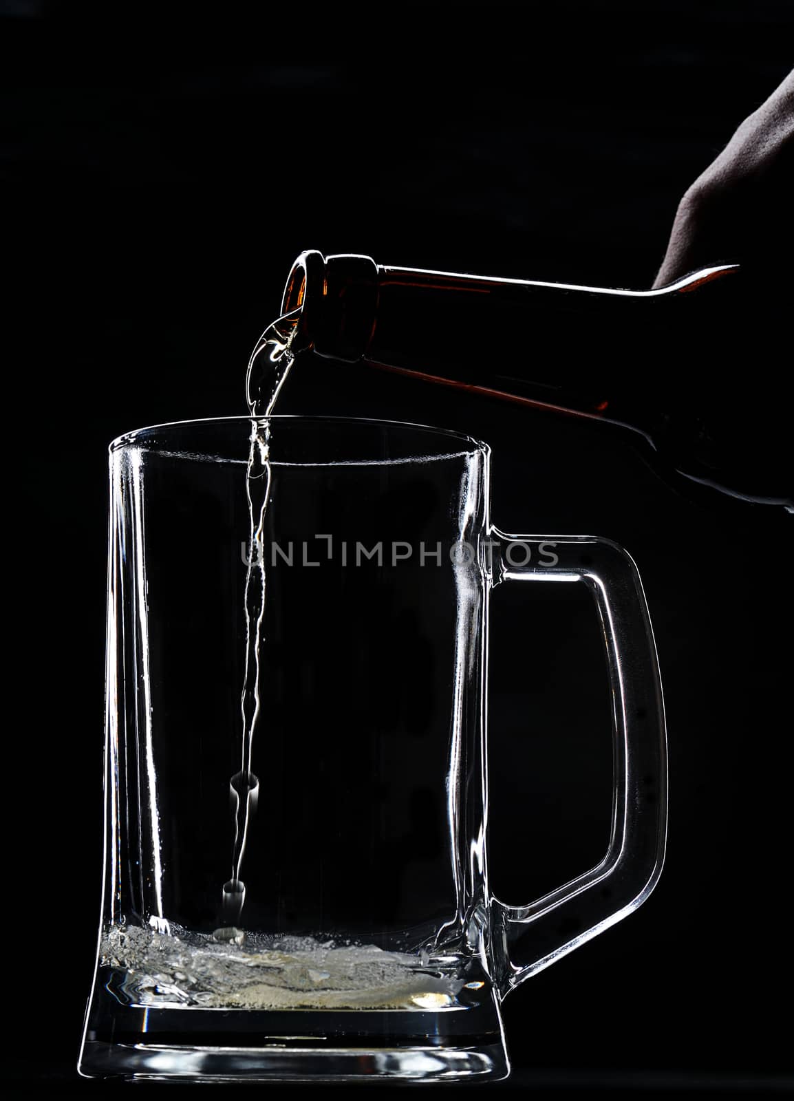 Pouring beer in empty glass from bottle on black background