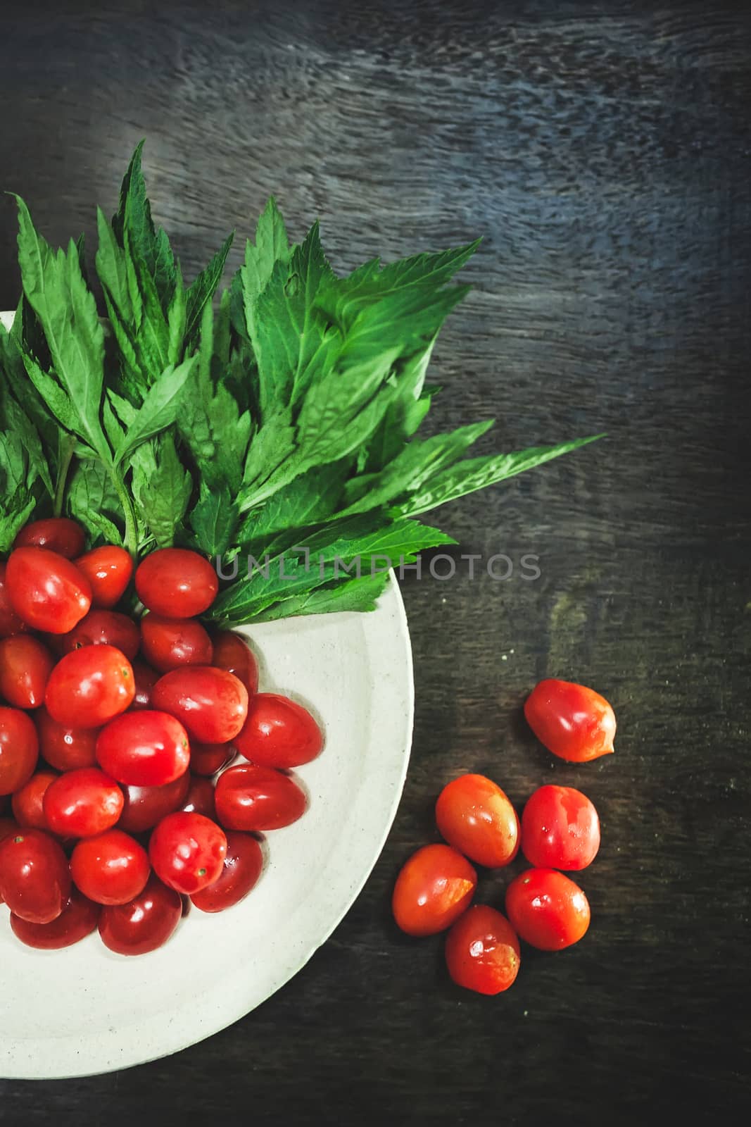 Small tomatoes and green vegetable on rustic black wooden background.
