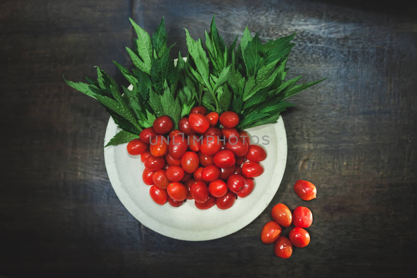 Small tomatoes and green vegetable on rustic black wooden background.