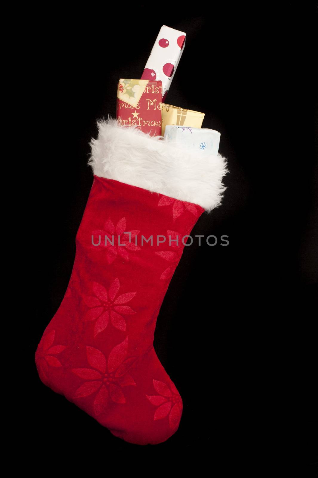 Colorful red Christmas stocking with decorative wrapped gifts peeking out the top over a black background with copy space