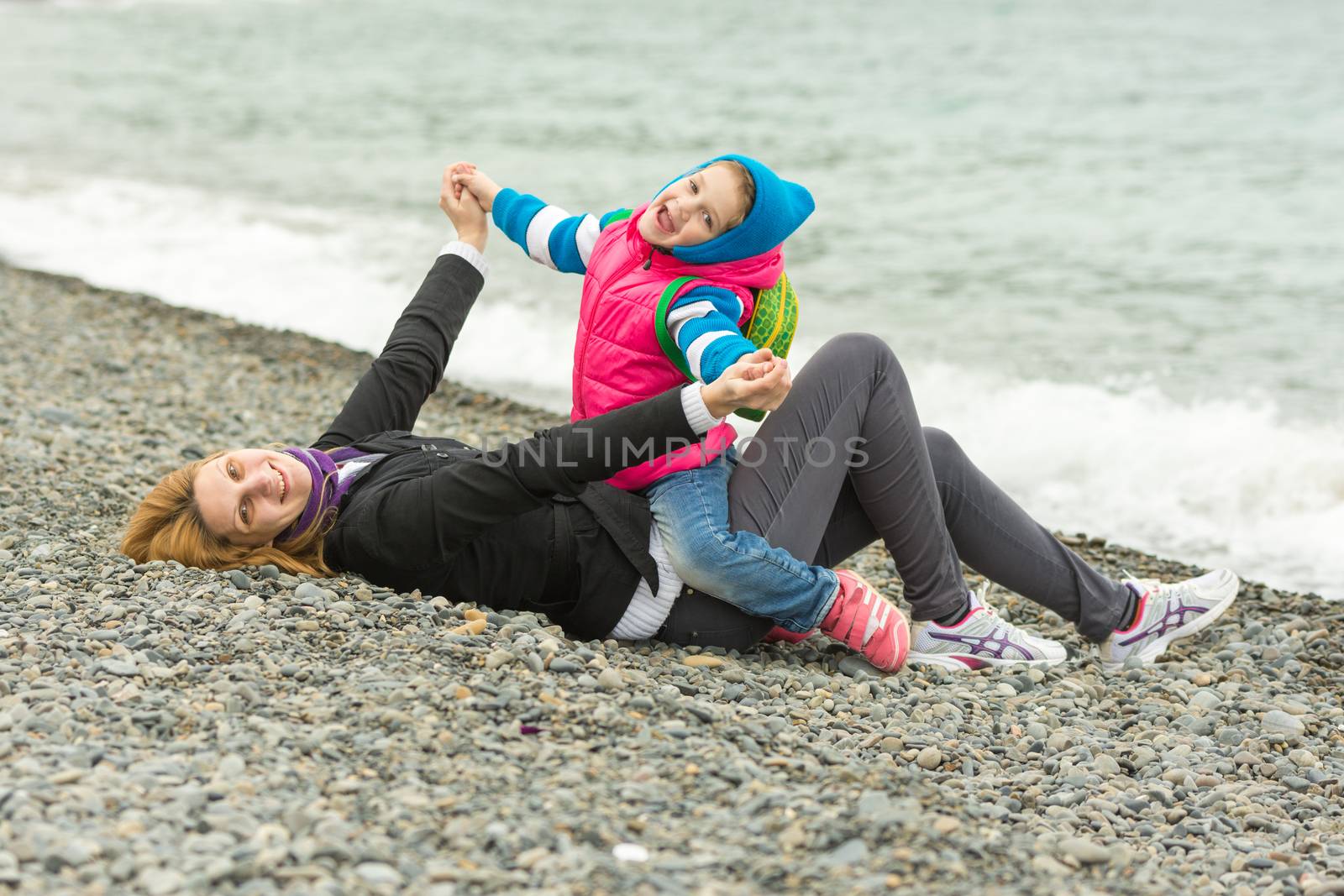 Five-year girl with her mother having fun on the beach pebble beach in cold weather