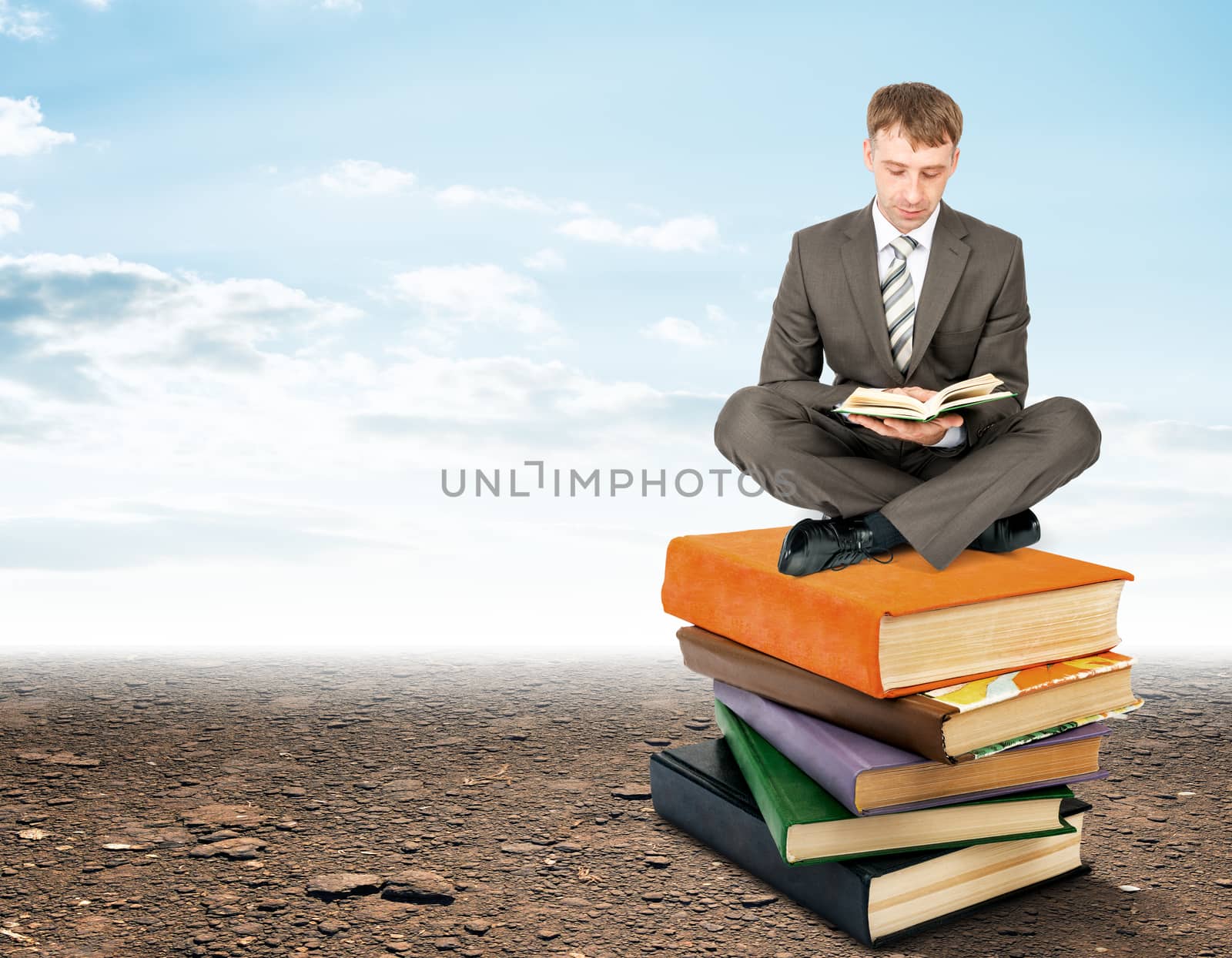 Businessman sitting on stack of books and reading by cherezoff