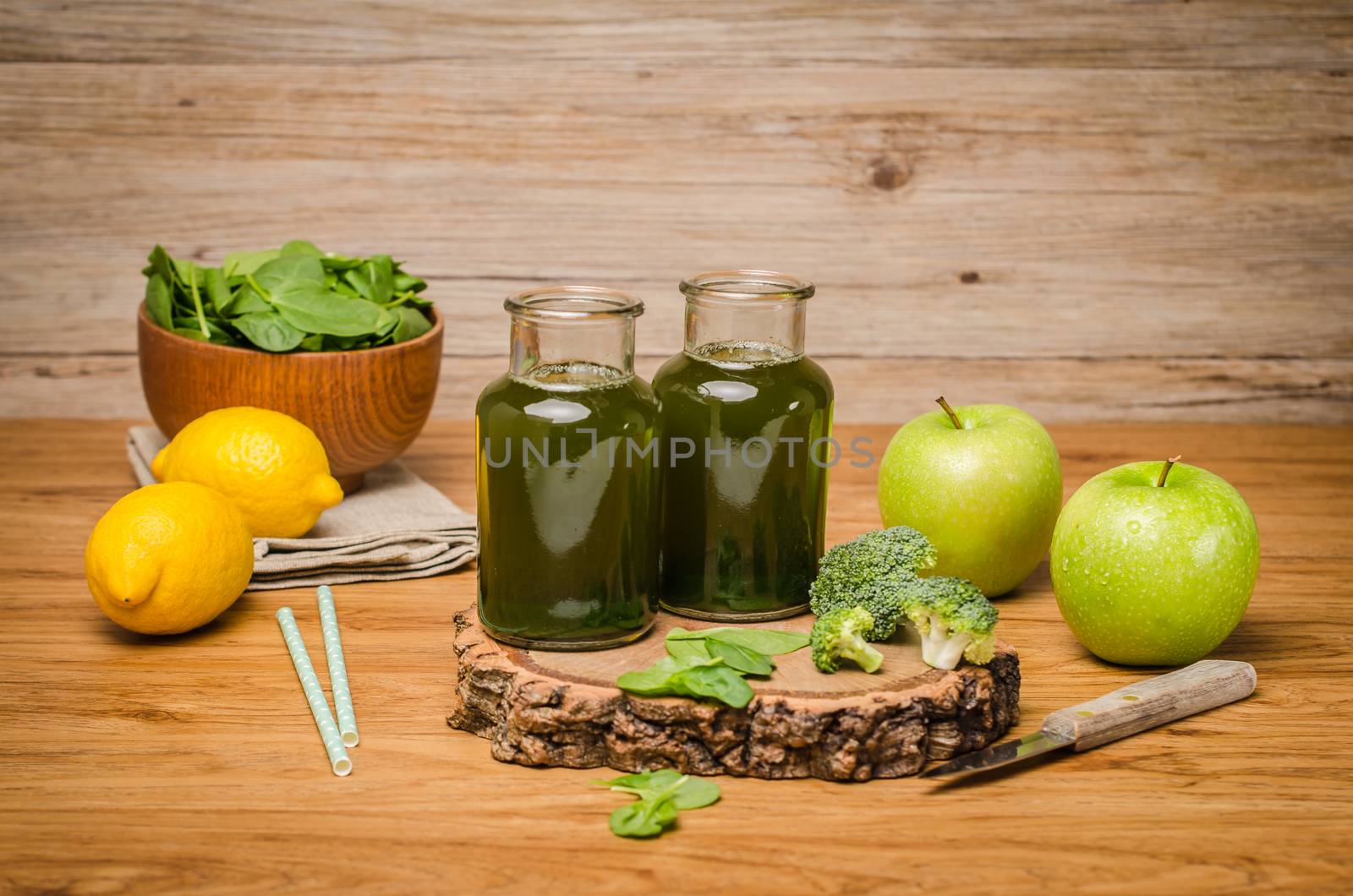 Green fresh leafy greens smoothie in glass jar, spinach leaves, apple, broccoli and lemon. Refreshing healthy drink on wooden table background