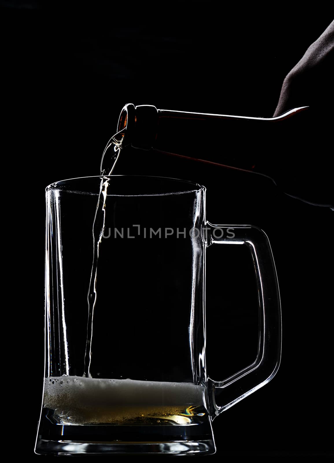 Serving beer in empty glass from bottle on black 