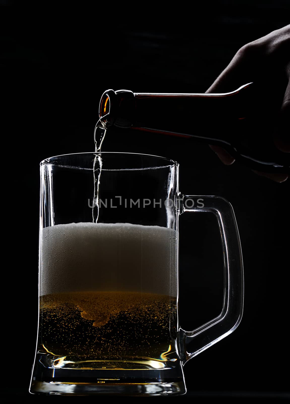 Pouring fresh beer from bottle on black