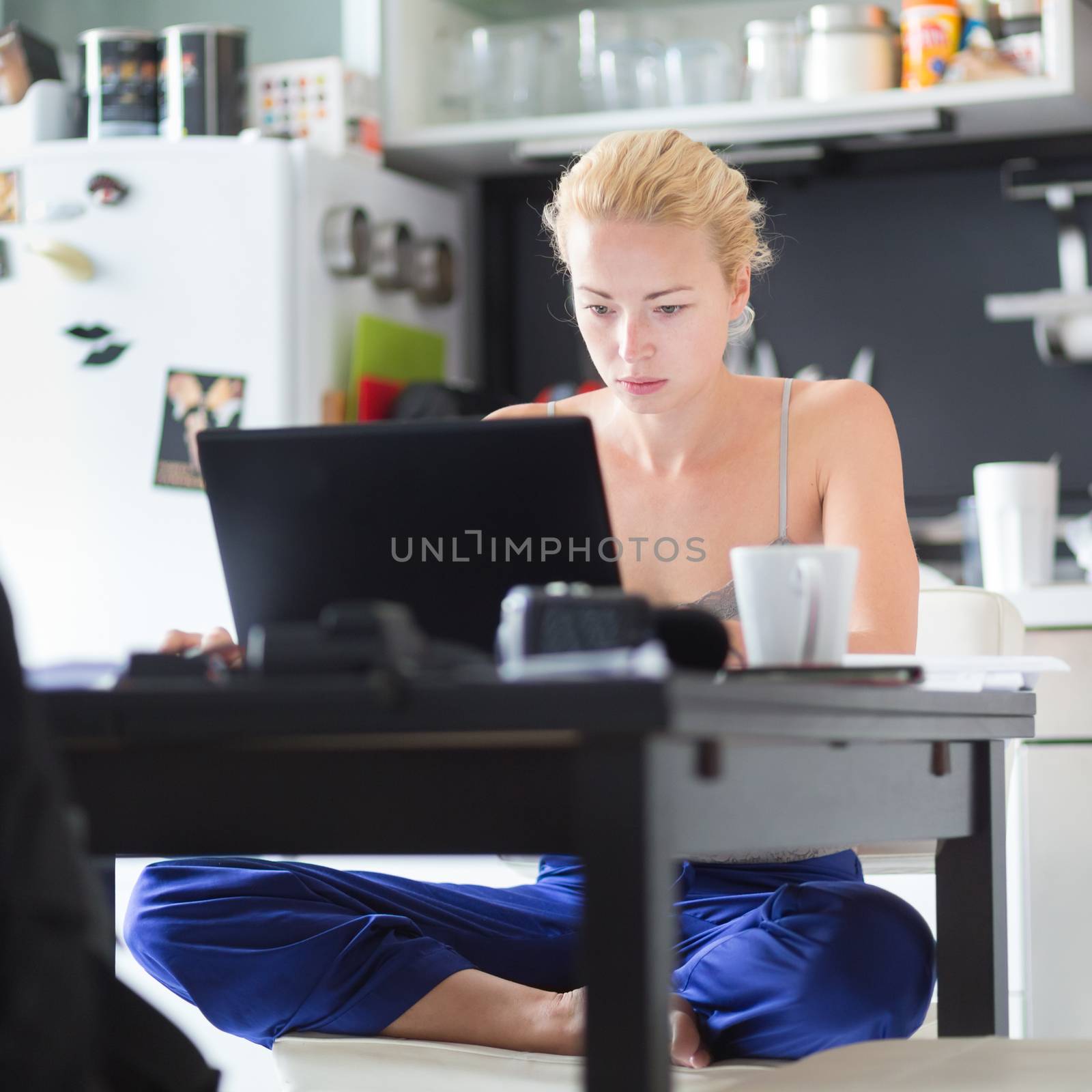 Female freelancer in her casual home clothing working remotly from her dining table in the morning. Home kitchen in the background.