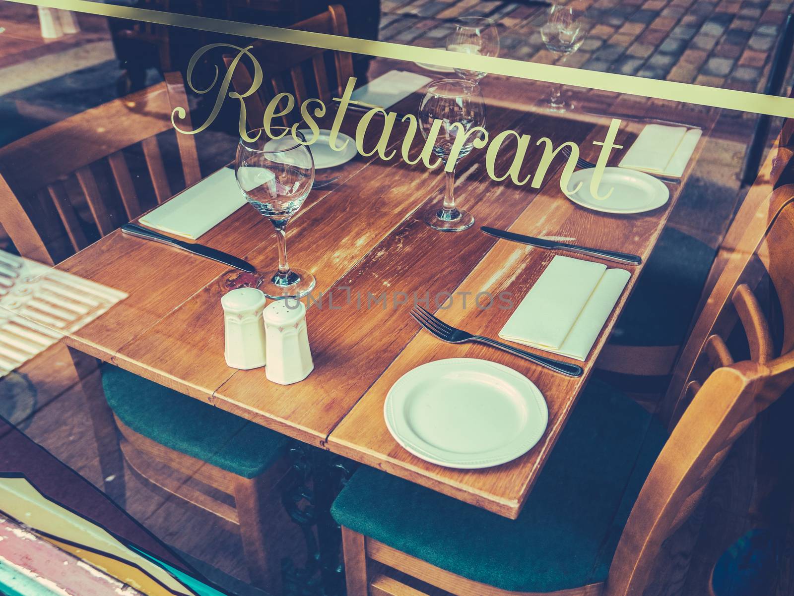 Retro Style Street Image Of A Rustic Restaurant Table Through A Window On A Cobblestone Street In Europe