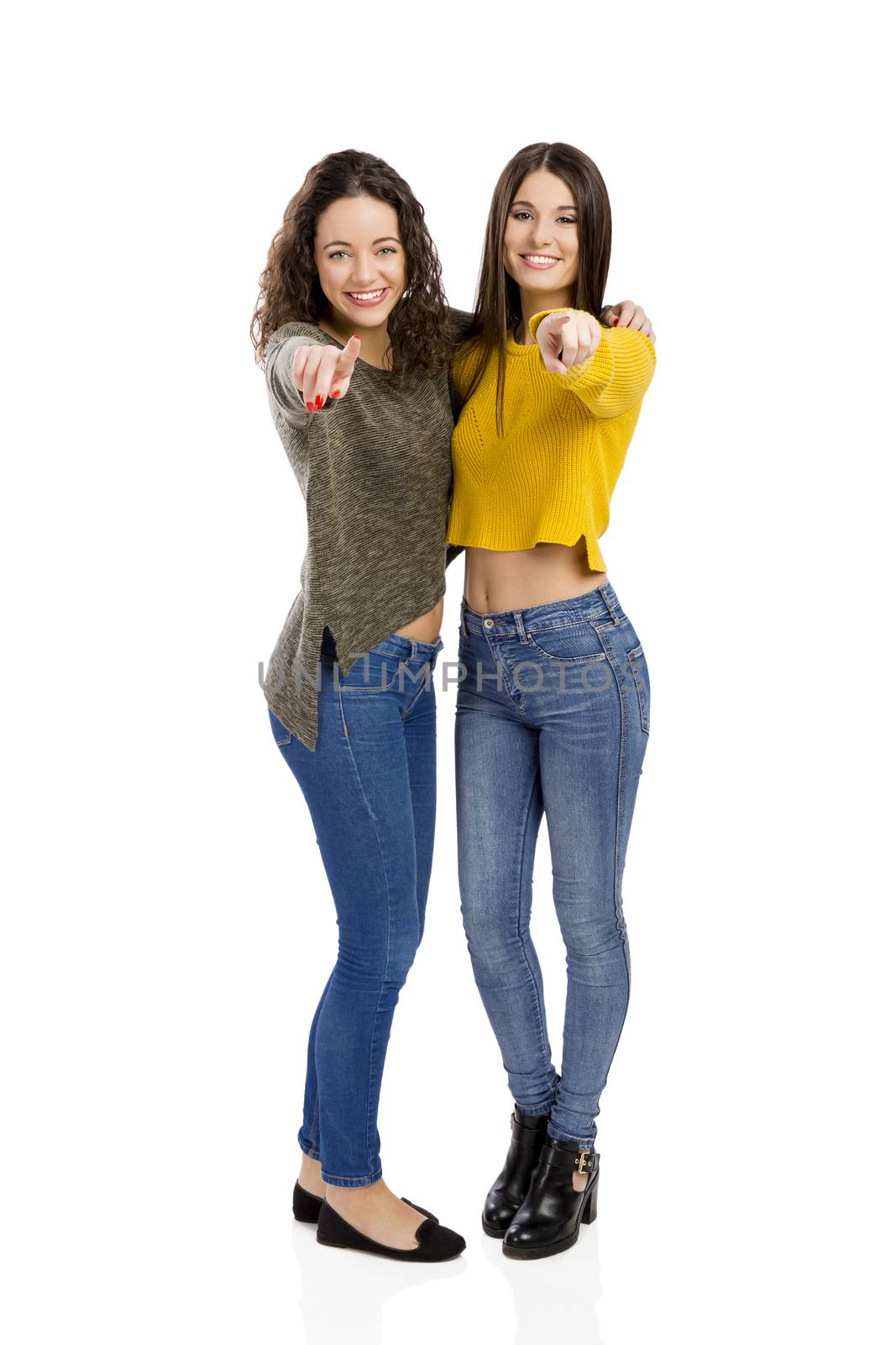 Studio portrait of two beautiful girls pointing and looking to the camera