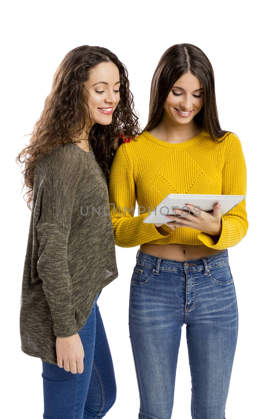 Studio portrait of two beautiful girls holding and showing something on a tablet