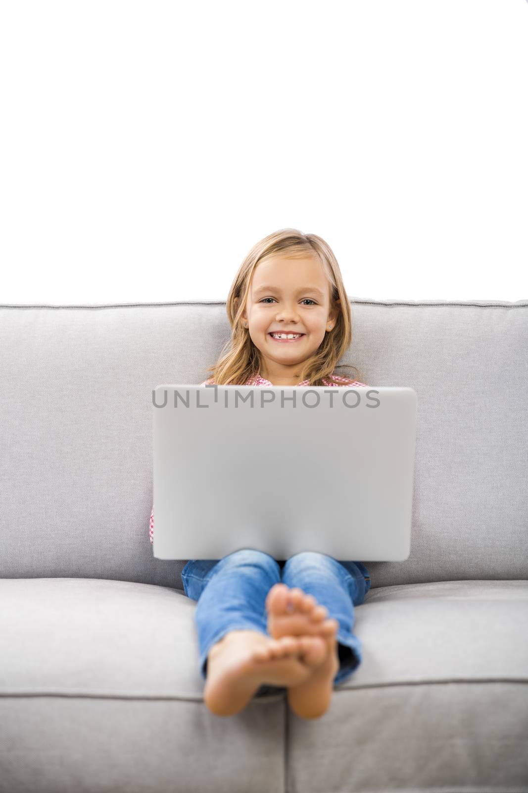 Happy little girl sitting on a couch and working a laptop