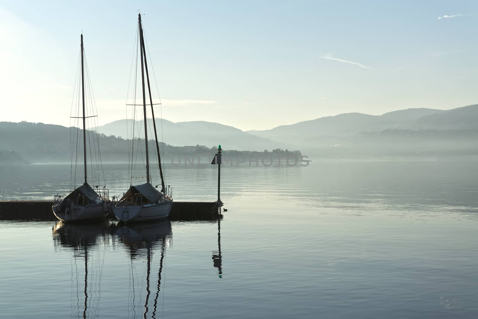 two boats in the harbor on a calm lake and the horizon mists of winter