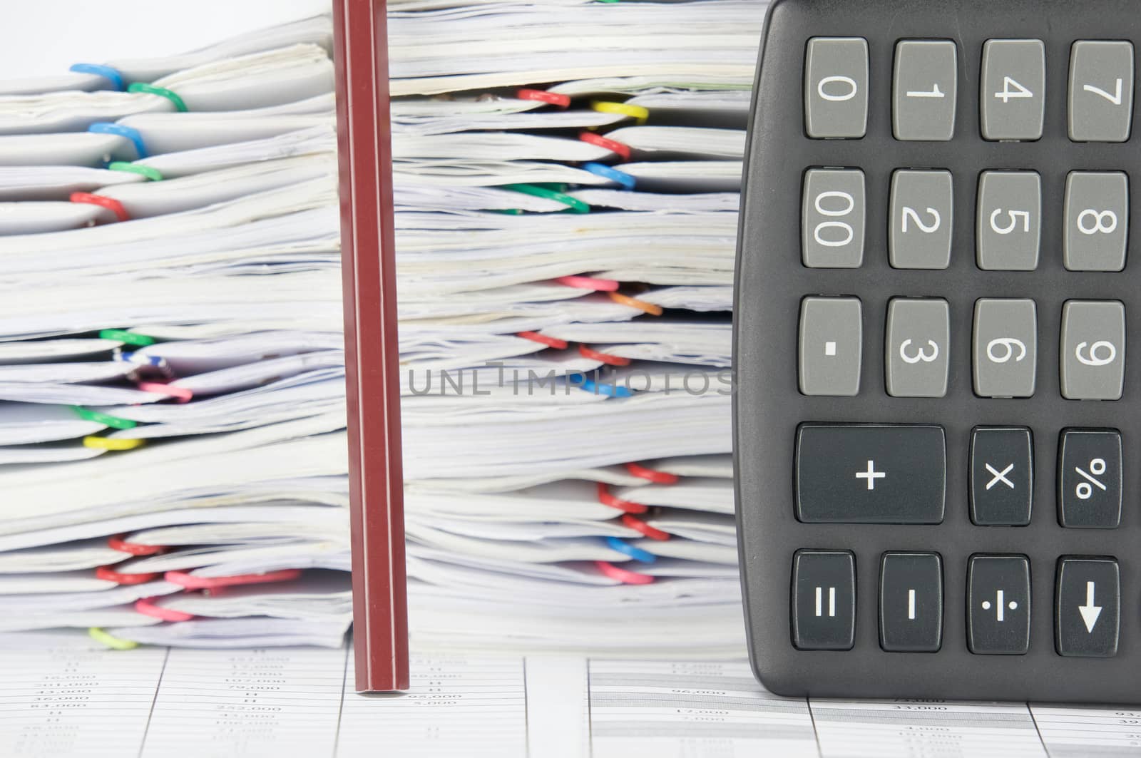 Brown pencil and calculator place vertical on finance account have overload of paperwork with colorful paperclip as background.