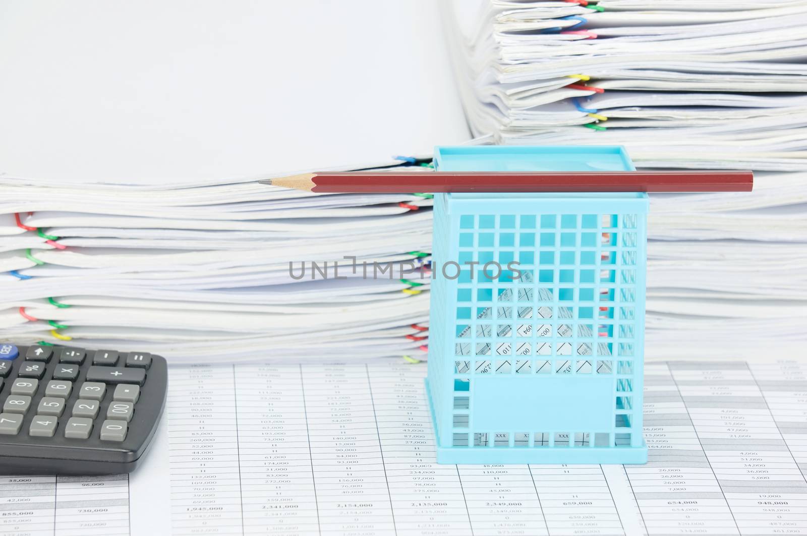 House in blue basket with brown pencil on top and calculator on finance account have overload of paperwork with colorful paperclip as background.