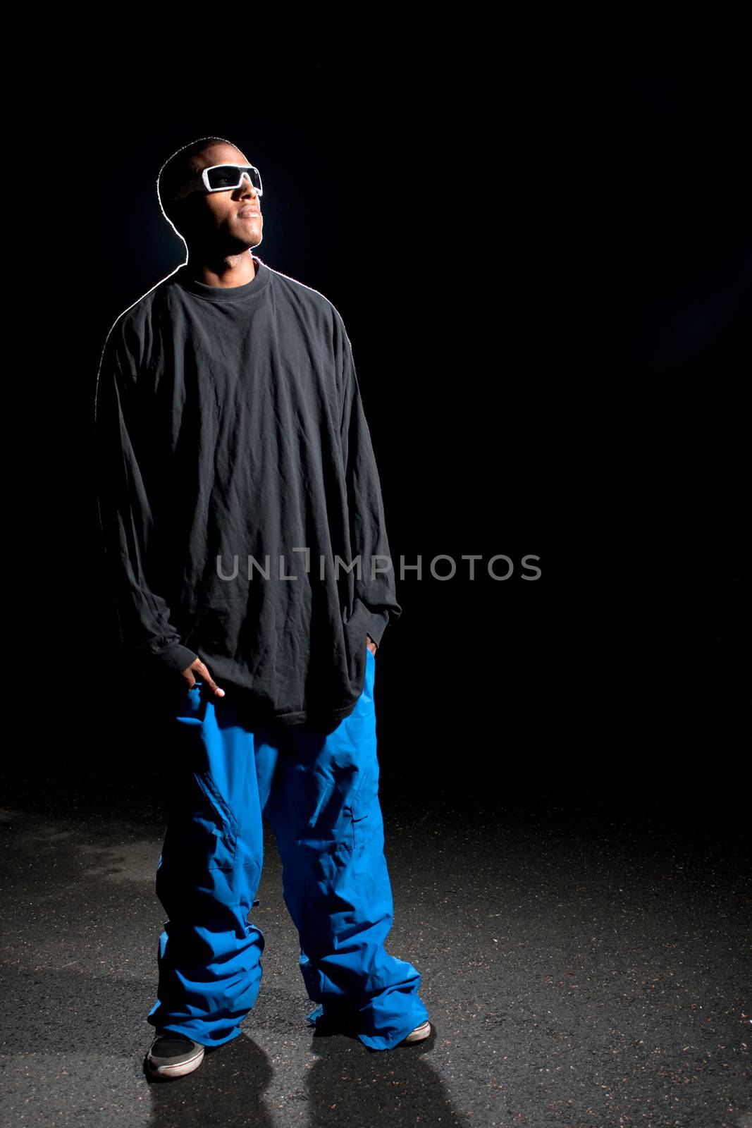 African American young man wearing baggy winter sports clothing posing under dramatic lighting with lens flare.