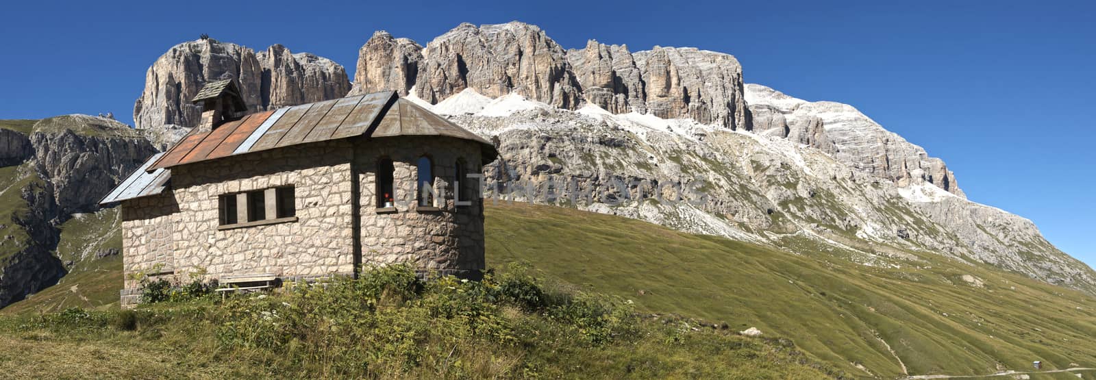 Church on the green grass at the foot of the massif of the Sella mountain range and blue sky in the background