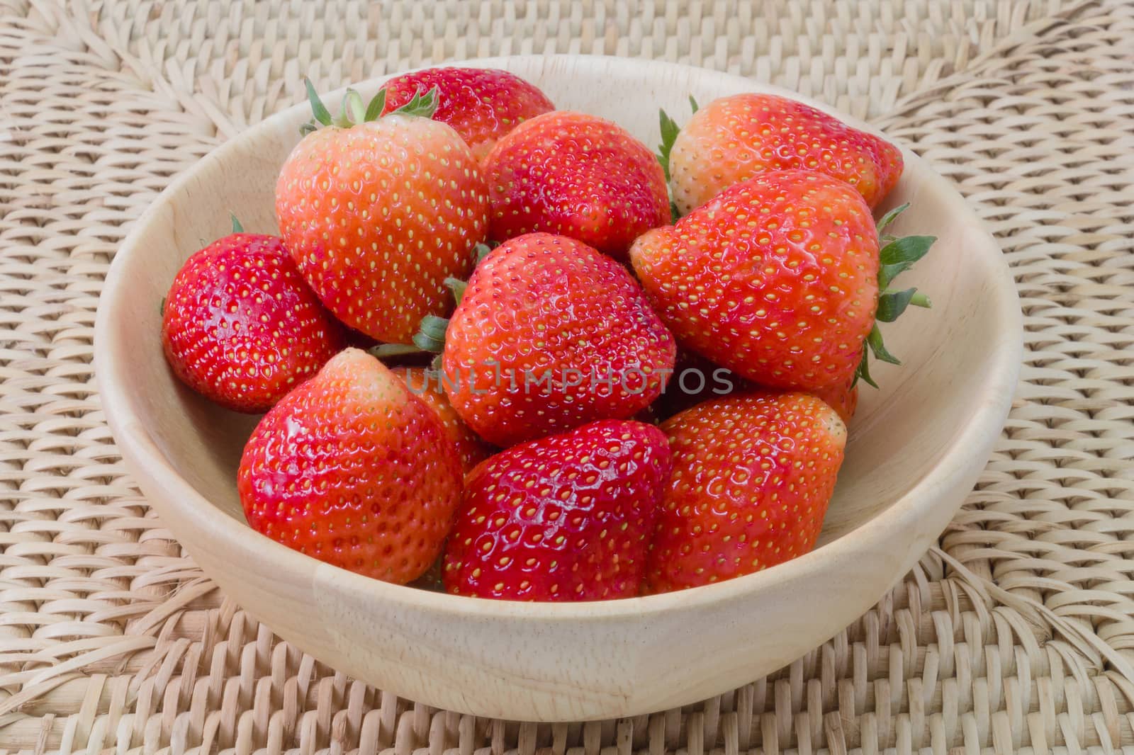 fresh strawberry in wooden bowl on wickerwork background by chingraph