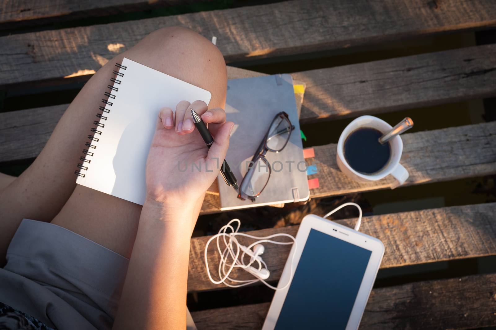 Young hipster woman writing journal on small notebook while sitting on wood litter in early morning time on weekend